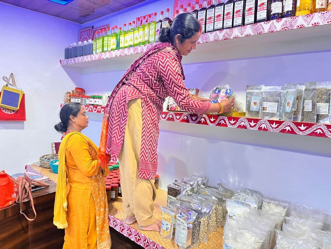 Women arranging packaged products made at a livelihood centre on a shop shelf