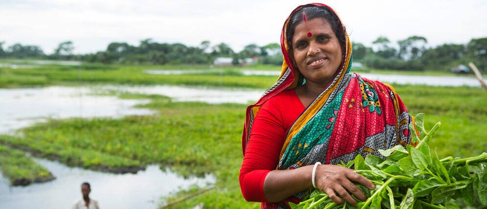 Woman farmer holding freshly picked leafy greens beside a wetland field